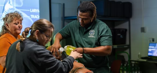 Three students practicing providing medical assistance to a medical dummy.